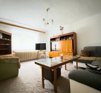 Obývací pokoj v rodinném domě s pohovkami, skříňkami a stolkem, kobercem na podlaze.