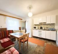 Kuchyně v rodinném domě se světlým nábytkem, jídelním stolem a posezením.