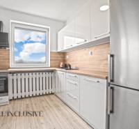 Bílá kuchyň v 2-pokojovém bytě s podlahou s dřevěným dekorem a výhledem z okna.