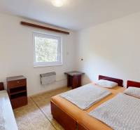 Ložnice v chatě se třemi lůžky, noční stolek a okno s výhledem.