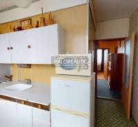 Kuchyně v 3-pokojovém bytě s bílými skříňkami a lednicí na podlaze s dřevěným dekorem.