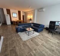 Obývací pokoj v dvoupokojovém bytě s modrou sedačkou a pracovním stolem.