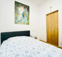 Ložnice s obrazem na stěně, postelí a nočním stolkem v dvoupokojovém bytě.