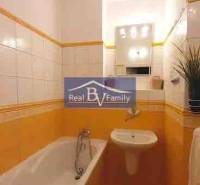 Koupelna v 2-pokojovém bytě s obkladem v teplých odstínech a vanou.