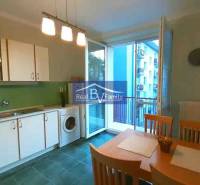 Kuchyně v 2pokojovém bytě s bílými skříňkami, jídelním stolem a balkónem.