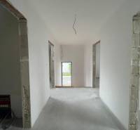 Interiér rodinného domu s bílými stěnami a otevřenými dveřmi do další místnosti.