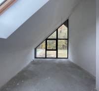 Podkrovní pokoj s velkými okny a vyvýšeným stropem v rodinném domě, bez podlahové krytiny.