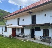 Venkovská chata s červenou střechou a terasou, obklopená zeleným trávníkem a přírodou.