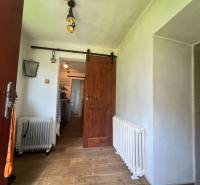 Interiér chaty s podlahou s dřevěným dekorem, radiátorem a posuvnými dřevěnými dveřmi.