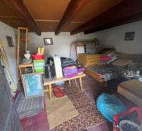 Interiér nepoužívané chaty s venkovským nábytkem a stropními trámy.