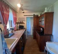 Kuchyně v dřevěné chatě s rustikálním nábytkem, umyvadlem a dekorativními záclonami.