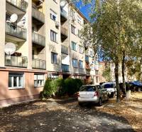 Bytový dům na Mederčské v Komárně se zaparkovanými auty a stromy.