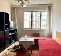 Obývací pokoj ve 3-pokojovém bytě s červenou pohovkou, koberec, starší televizor, prosvětlený prostor.