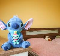 Pokoj ve 4pokojovém bytě se žlutými stěnami, hračkami a postelí s růžovým přehozem.