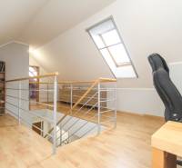 Podkrovní část 4pokojového bytu s pracovním křeslem a knihovničkou, podlaha s dřevěným dekorem.