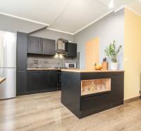 Kuchyně ve 4-pokojovém bytě s ostrůvkem, černými skříňkami a podlahou s dřevěným dekorem.