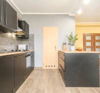 Kuchyně ve 4-pokojovém bytě s černými skříňkami a podlahou s dřevěným dekorem.