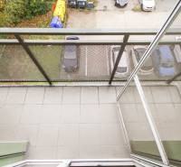 Balkon ve 4-pokojovém bytě s výhledem na parkoviště a zeleň.