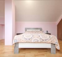 Světlá ložnice, podlaha s dřevěným dekorem, strop se sklonem, pohodlná postel, úložný prostor.