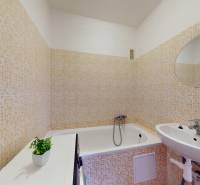 Koupelna v 1-pokojovém bytě s obklady, vanou a zrcadlem.