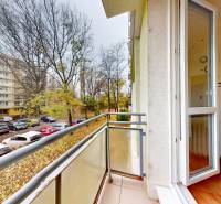 Balkon v Bratislavě na Exnárově ulici, s výhledem na parkoviště a stromy.