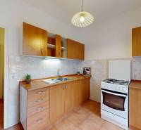 Kuchyně v 1-pokojovém bytě s dřevěnými skříňkami, bílým sporákem a světlem na stropě.