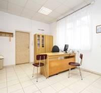 Kancelář s dřevěným nábytkem, počítačem a dekoracemi na stěnách, dlažba na podlaze.