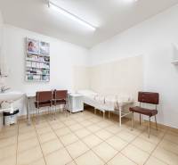 Místnost v kanceláři s dlažbou, umyvadlem, židlemi a lehátkem.