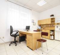 Kancelář s počítačem, stolem a židlí, světlý interiér, police a umyvadlo.