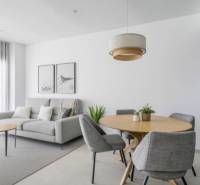 Světlý obývací pokoj rekreačního apartmánu se šedým křeslem a dřevěným stolem.