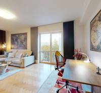 Obývací pokoj v 2pokojovém bytě s pohovkou, pracovním stolem a podlahou s dřevěným dekorem.