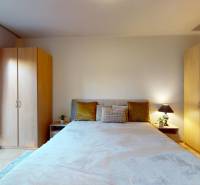 Ložnice v dvoupokojovém bytě s dvojlůžkem, skříněmi a výhledem na balkon.