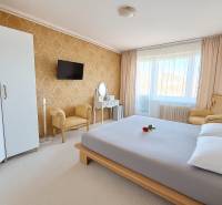 Ložnice v 3-pokojovém bytě s elegantním nábytkem, zlatou tapetou a bílým kobercem.