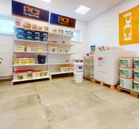 Obchodní prostory se stavebním materiálem, regály s vědry, podlaha s dřevěným dekorem.