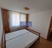 Ložnice v dvoupokojovém bytě s postelí, závěsy a podlahou s dřevěným dekorem.