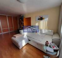 Světlý obývací pokoj v 2-pokojovém bytě s podlahou s dřevěným dekorem a bílou sedačkou.