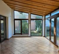 Pokoj v rodinném domě s velkými okny a dlažbou, výhled do zahrady.