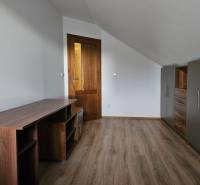 Pokoj v rodinném domě s nábytkem, bílými stěnami a podlahou s dřevěným dekorem.