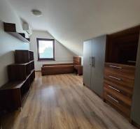 Podkroví rodinného domu s nábytkem, podlahou s dřevěným dekorem a oknem.