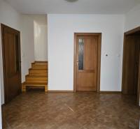 Interiér rodinného domu s keramickou dlažbou, dřevěné schody a dveře s prosklením.