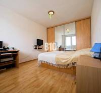 Ložnice v 2-pokojovém bytě s podlahou s dřevěným dekorem, zrcadlovou skříní a pracovním stolem.