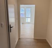 Garsonka s podlahou s dřevěným dekorem a velkými okny poskytuje světlý interiér.