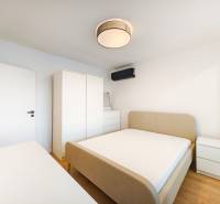 Ložnice v 2pokojovém bytě s postelí, skříní, komodou a podlahou s dřevěným dekorem.