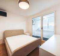 Ložnice v 2-pokojovém bytě s postelí, stolkem a balkonem, podlaha s dřevěným dekorem.