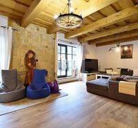 Interiér chaty s kamennou stěnou, velkou pohovkou a podlahou s dřevěným dekorem.