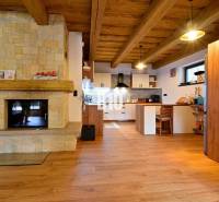 Interiér chaty s kachlovými kamny, dřevěným stropem a podlahou s dřevěným dekorem.