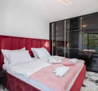 Ložnice ve vile s postelí čalouněnou červeným sametem a skleněnou skříní.