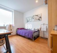 Ložnice ve 4pokojovém bytě s podlahou s dřevěným dekorem a fialovým přehozem.