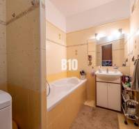 Koupelna se žlutými obklady, vanou, umyvadlem a úložným prostorem ve 4pokojovém bytě.