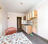 Kuchyně s jednoduchými skříňkami, kachličkami a stolem v rodinném domě.